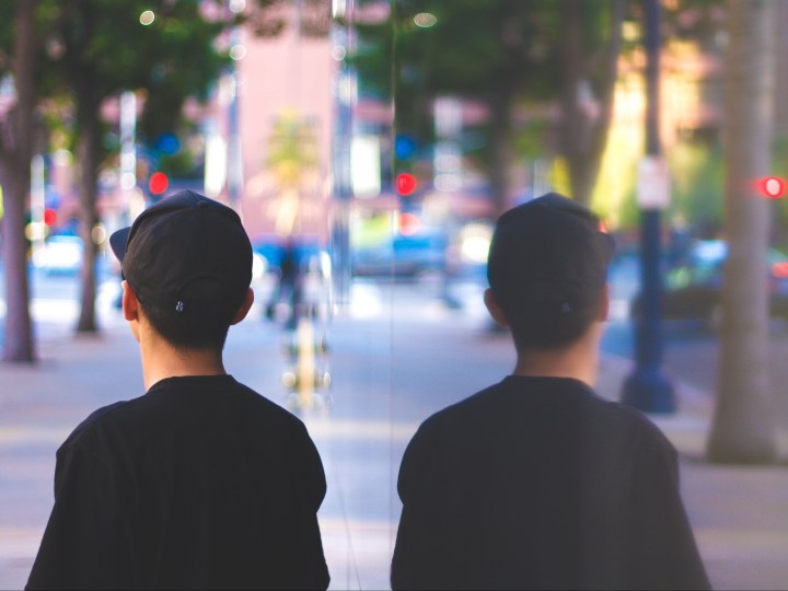 Man shown from behind next to a window with his reflection